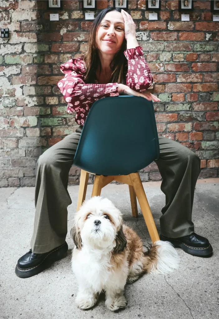 A relaxed woman in a floral top, enjoying time with her dog in a contemporary space.
